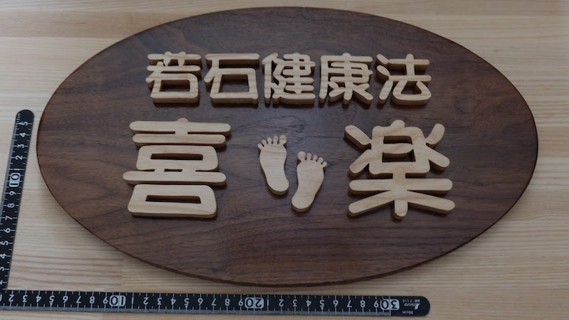 ウォルナットの楕円形の板にホワイトアッシュの切文字を載せた木製看板。